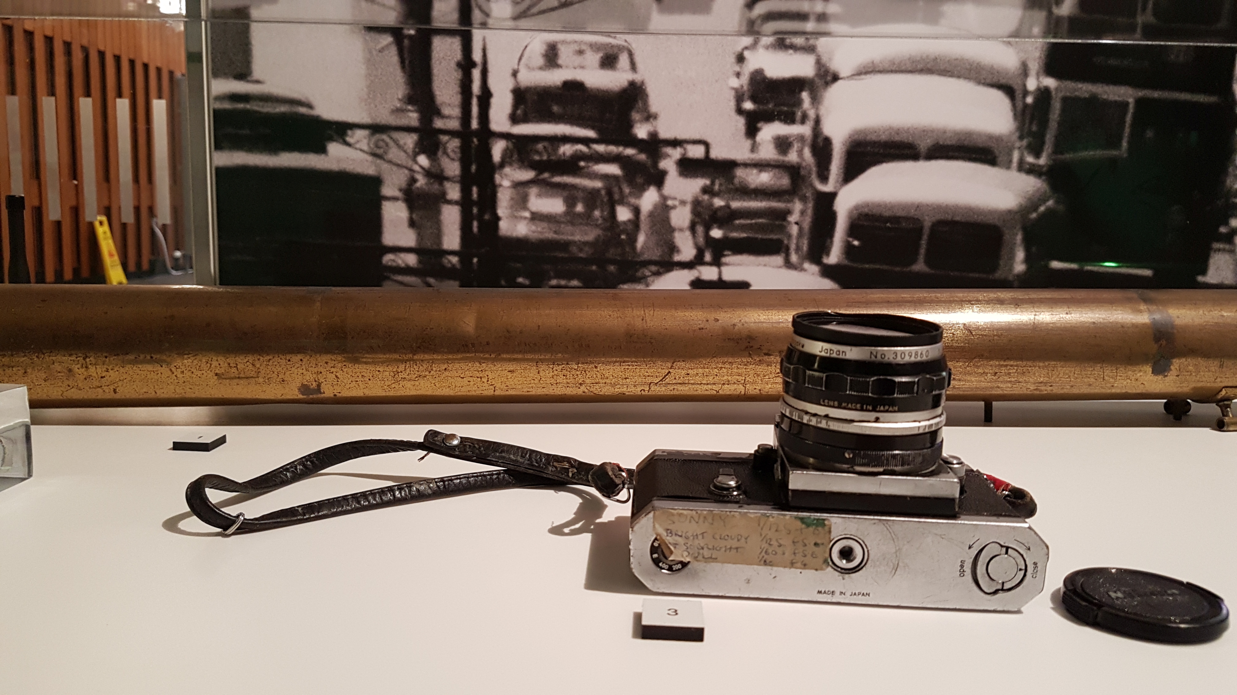 A Nikon SLR camera laid on its side with a handwritten label of settings visible on the baseplate.