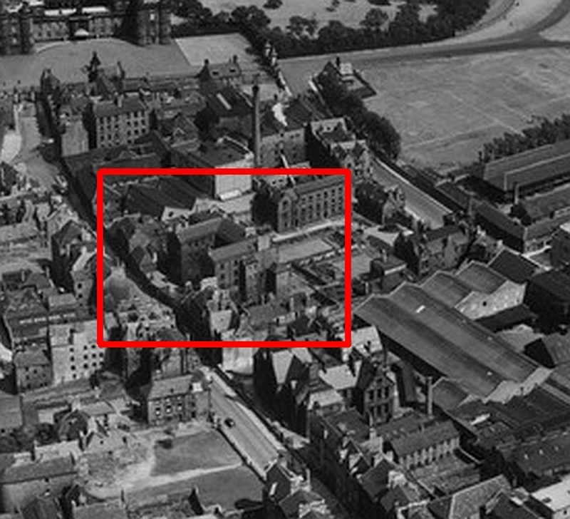 An aerial photograph with a grim building highlighted in red with pleasant gardens behind it.