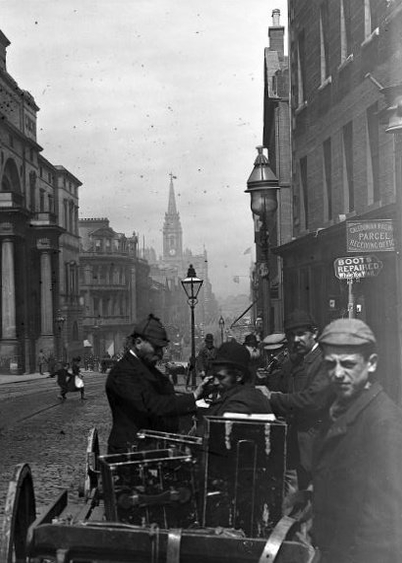 A group of male photographers with their equipment on handcarts by the site of a city street.